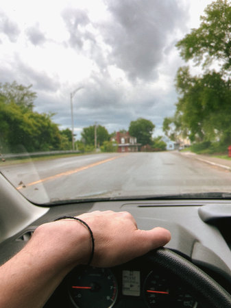 View from the inside of a car on the road and man's hand on the steering wheel
