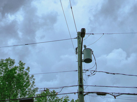 Blue sky with white clouds and electric pole with wires and cables.