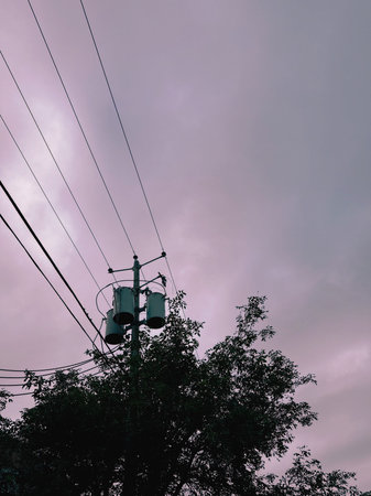 Electric pole with power lines and wires against a cloudy sky. Sunset.