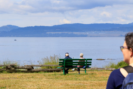 Senior couple sitting on a bench on a sea shore looking at the horizon in Victoria, BC, Canada