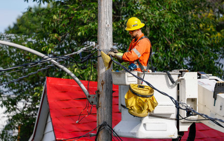 Electrician working on a power line with an electric pole in the background. A worker works on...