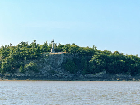 View from the sea to the island of Grosse Isle. Cross on the top of a hill in Grosse Isle, Quebec.