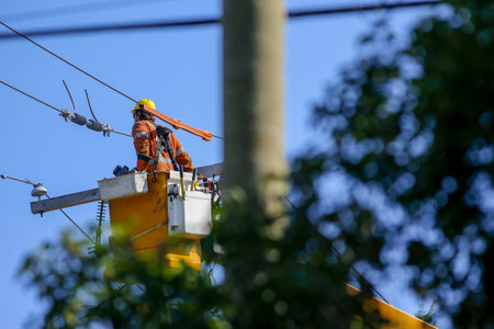 Electrician working on a power pole with a jackhammer in the background. Aworker works on electrical...