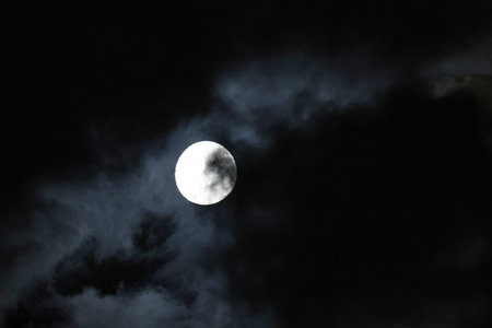 Full moon in the night sky with dark clouds, closeup of photo