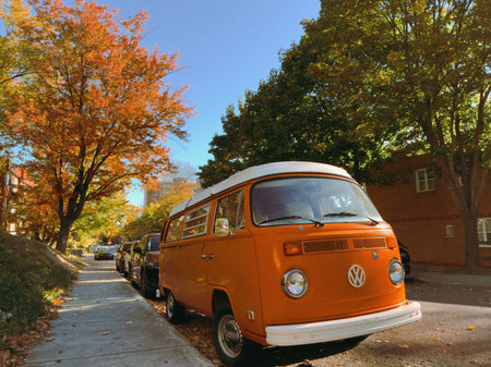 Old orange Volkswagen Westfalia van parked on a residential street in autumn.