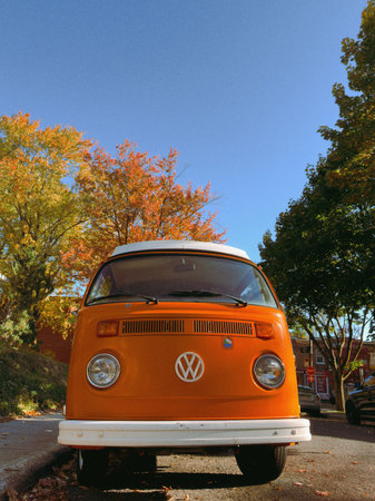 Old orange Volkswagen Westfalia van parked on a residential street in autumn.