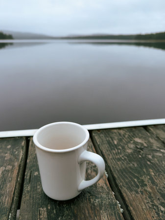 Coffee mug on a wooden pier with a lake in the backgroundの写真素材