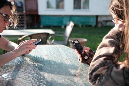 Young woman and her mother using their mobile phone outside.