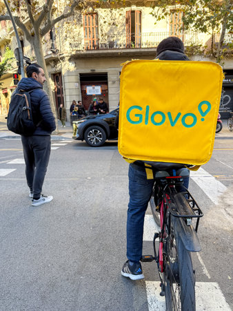 Glovo food delivery by bicycle in the streets of Barcelona, ââââSpain. Delivery man rides a bicycle in the street in Barcelon.のeditorial素材