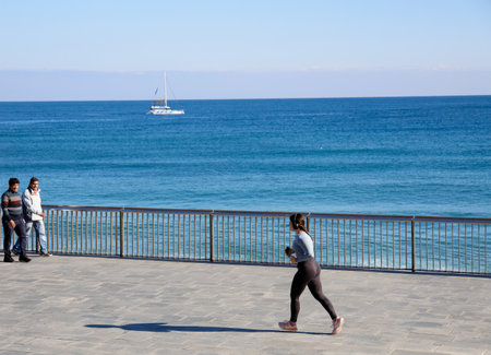 Barcelona, Spain. People stroll along the beach promenade in Barcelona. A woman who is jogging.のeditorial素材