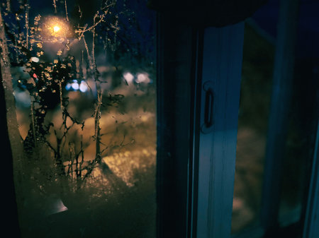 A view from the window of the house at night with a snowfall. Frosty pattern on the window. Winter background.の写真素材