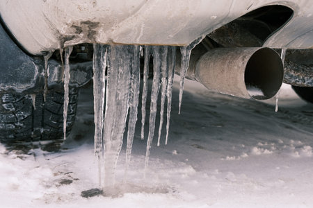 Icicles hanging from a car in winter. 
Car exhaust pipe in winter.