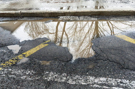 Broken asphalt road with potholes and yellow marking lines. Pothole in the street in spring.の写真素材
