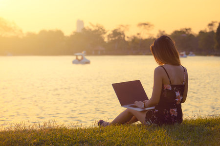 attractive women using laptop in park during sunset . Thailand , Southeast Asiaの写真素材