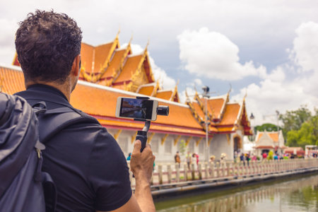 Man backpacher who holds mobile phone on gimbal visiting Asia during a sunny day , Solo trip ,...
