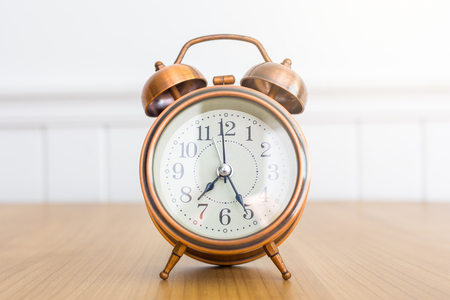 Vintage alarm clock on wooden table over white wall background during dayの写真素材