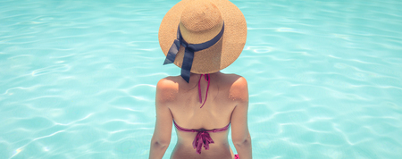 Woman with brown hat relaxing in swimming pool with blue water during a sunny day , holiday conceptの写真素材