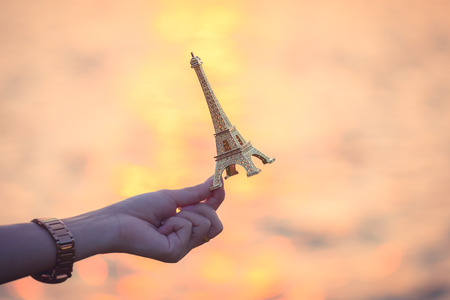 Hand holding a miniature Eiffel tower during sunset . french culture .の写真素材