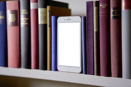 Upright standing mobile phone screen between colorful books in a shelfの写真素材
