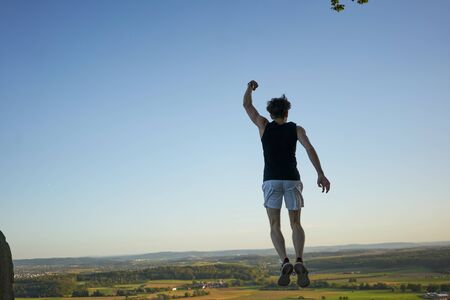 Sporty man jumping on a hill in front of beautiful landscape and viewの写真素材