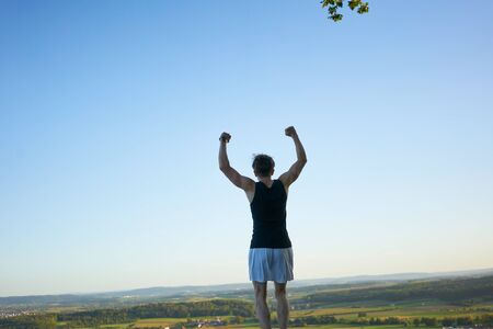 Sporty man jumping on a hill in front of beautiful landscape and viewの写真素材
