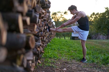 Athlete in muscle shirt stretching his leg on woodpileの写真素材