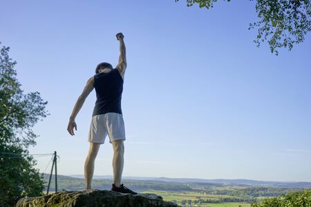 Athlete in tanktop on top of mountain raising his arm with fist on rock.の写真素材