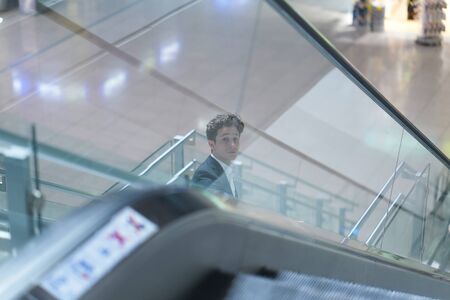 Young attractive businessman going down on an escalator in the airport, looking upの写真素材