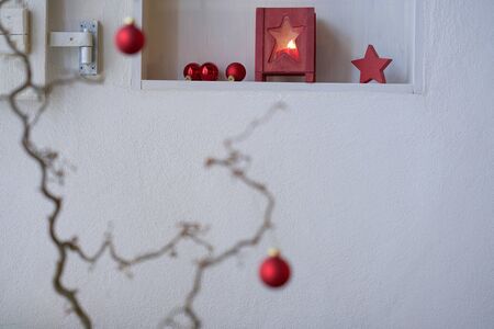 Unsharp red christmas balls at a branch in front of a shelf with red christmas decoration, lantern with candle light, red starの写真素材