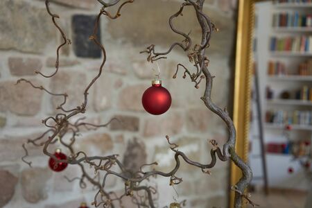 Close up of red christmas decoration at a branch in front of unsharp stone wall and mirror with reflections in a loft apartmentの写真素材