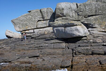 Big rock formation at the shore of Brittany, mother and child standing on the rocks, blue skyの写真素材