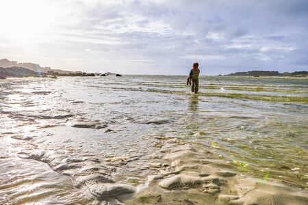 Active children in rainwear standing in the low water of the sea at a beach, beautiful light reflectionsの写真素材