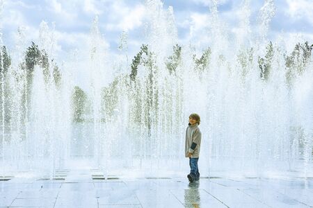 Smiling happy handsome boy standing in front of a big fountain in a city, sprayの写真素材