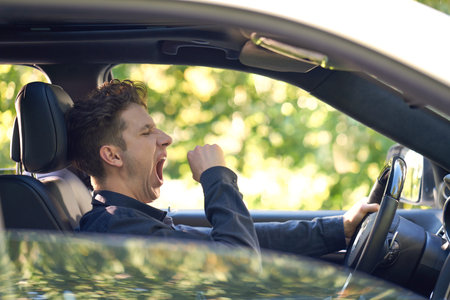 Young tired driver sitting in his car and yawning.