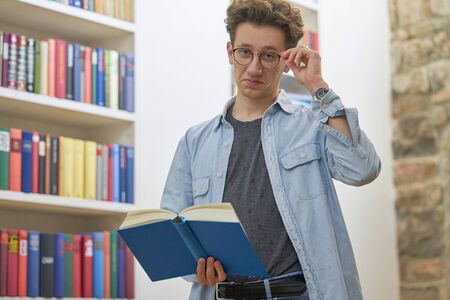 Young proud student, looking mischievously into the camera and touching his glasses.の写真素材
