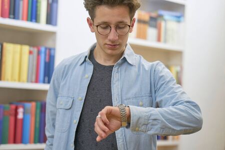 Student in library, checking the time on his watch.の写真素材