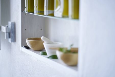 Still live bright and sunny detail of shelf in kitchen blurred in house with bottles olive oil wooden bowl mortar green mediterranean style moodの写真素材