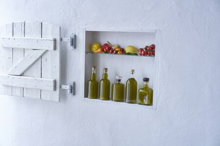 small shelf on the wall with bottles bottle olive oil and vegetables tomatos lemon paprika and garlic,old house apartment modern living barn shutter country style moodの写真素材