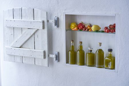 small shelf on the wall with bottles bottle olive oil and vegetables tomatos lemon paprika and garlic,old house apartment modern living barn shutter country style moodの写真素材