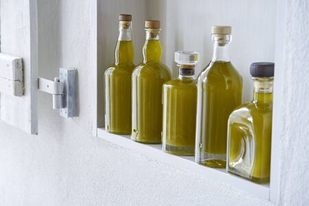 five bottles organic fresh healthy olive oil standing in a shelf in a country style house, gold yellow color and ambiance moodの写真素材