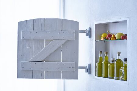modern living hous detail shutter,small shelf on the wall with bottles bottle olive oil and vegetables tomatos lemon paprika and garlic,old house apartment barn country style moodの写真素材