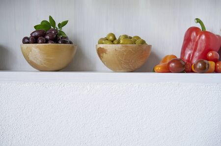 still life olives green brown and black in bowl with vegan red vegetables like tomatoes and paprika, white wall copy space vitaminsの写真素材