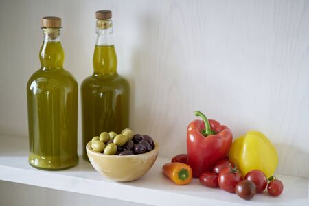 two wonderful bottles of cooking oil or olive oil on a wall shelf, wooden bowl with olives green and black next to vegan vegetarian vegetables such as tomatoes and peppers in Spainの写真素材