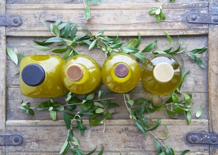 Closeup from above of four glass bottles oil golden liquid on a rustic shabby coffer surrounded by olive leaves mediterranean cooking house hotel restaurantの写真素材