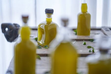 glass bottles filled with a golden liquid oil juice healthy organic vegan on a rustic wooden piece of furniture olive leaves around them in a mediterranean house sharp unsharp wellnessの写真素材