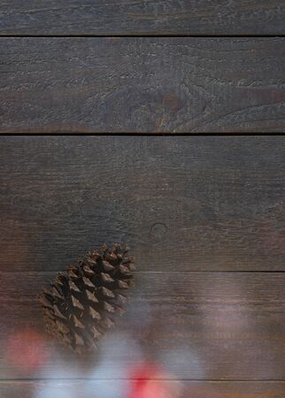 Christmas card with a fir cone and beautiful colourful christmas lights in front of a wooden backgroundの写真素材