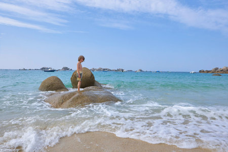 Happily laughing boy standing on rocks in the water of the sea, posing for the camera, summer holidaysの写真素材