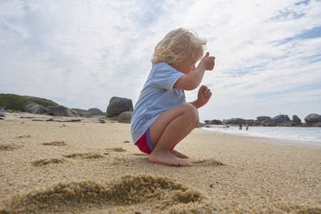 Cute little boy sitting in the sand of a beach, imitating taking a picture of the seaの写真素材