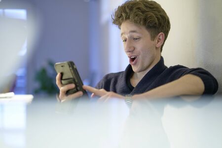 Young man being happily surprised while looking at his mobile phone in his handsの写真素材