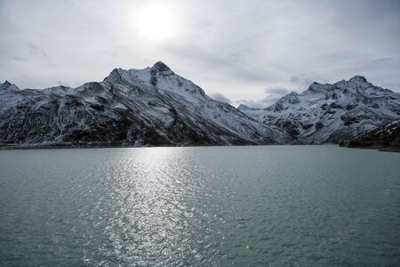 Water of a mountain lake with snowy hilltops in the background in evening lightの写真素材